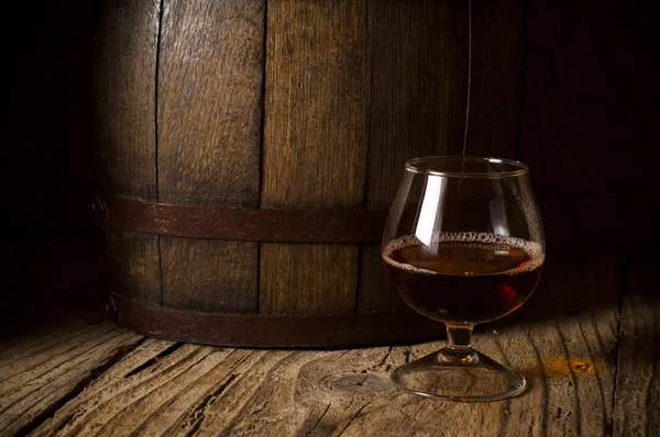 Glasses of brandy in cellar with old barrels — Stock Photo, Image