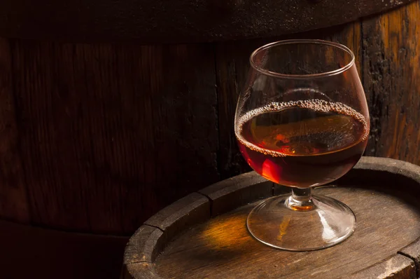 Glasses of brandy in cellar with old barrels — Stock Photo, Image