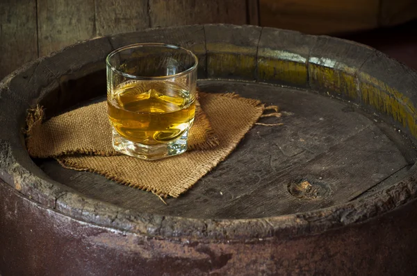 Glass of brandy in the cellar with old barrels stacked — Stock Photo, Image