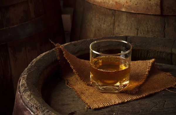 Glass of brandy in the cellar with old barrels stacked — Stock Photo, Image