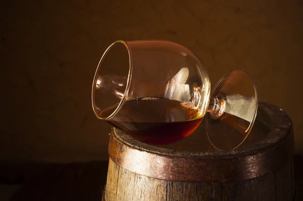 Bicchiere di brandy in cantina con vecchie botti impilate — Foto Stock