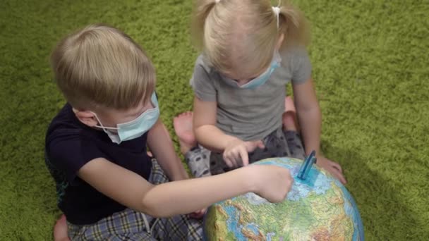 Gyerekek, egy lány és egy fiú orvosi maszkban forgatják a világot.