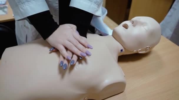 Een meisje in een witte jas oefent eerste hulp op een etalagepop, close-up in beweging, alleen handen zonder gezicht — Stockvideo