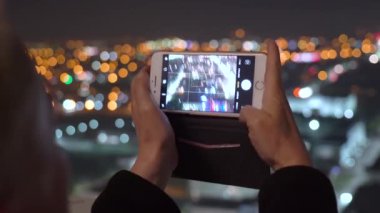Adam gece güzel bir şehir manzarasının arka planında yatay bir akıllı telefon tutuyor. İnsanlar ve teknoloji. Yakın plan..
