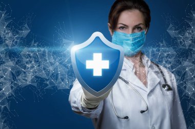 Hasta sağlığı koruma konsepti. Doktor mavi arka planda haçı olan koruyucu bir kalkan gösteriyor..