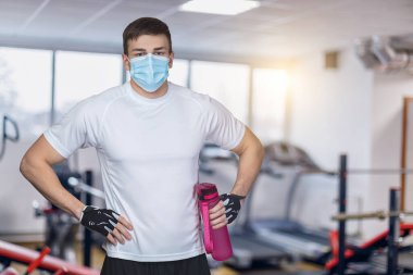 Genç koç spor salonunun arka planında maske takıyor..
