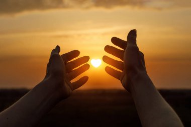 Kalp şeklinde güneşli bir gün batımı ve gökyüzünde eller havaya..