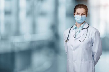 Koruyucu maskeli doktor bulanık bir arka planda duruyor..