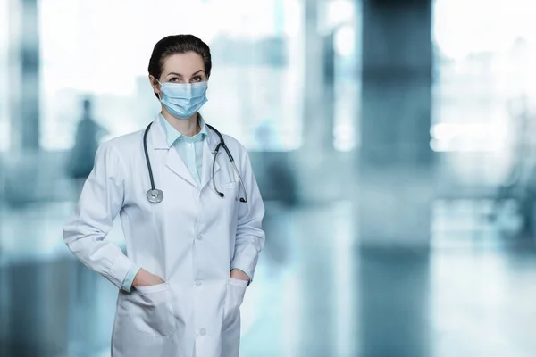 A medical professional in a mask stands on a blurred background.