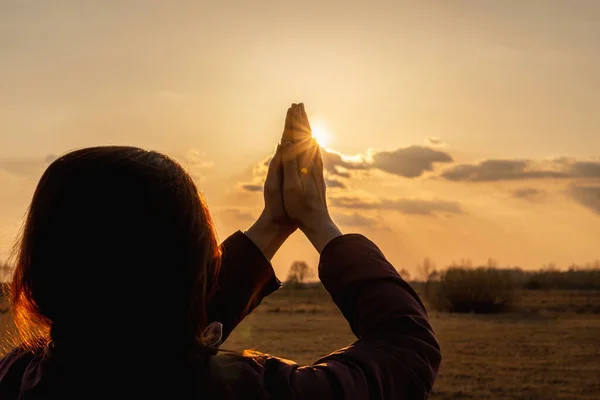 Woman stands with raised hands and prays against the background of sunset.