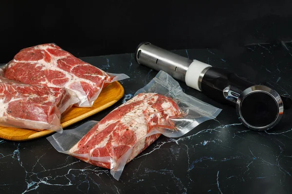 Meat in bags and sous vide devices on a black background.