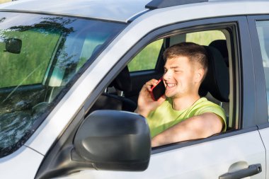 Genç bir adam direksiyonda oturur ve telefonda konuşur..