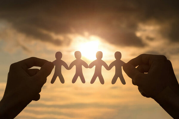 Руки держат группу порезанных бумагой людей на фоне солнца.