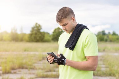 Genç sporcu, bulanık bir arkaplanda telefona bakıyor..