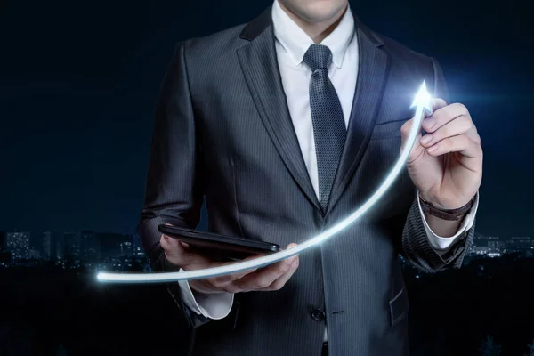 Business man draws a sharp rise in the form of an arrow on a blurred background.