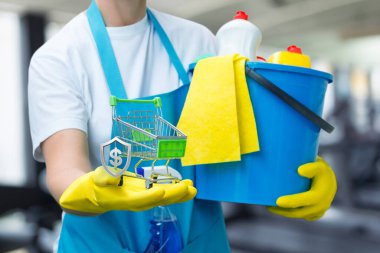 Spor salonu temizlerken eldiven giyip gülümsüyorsun. Eldivenli bir adam temizlik kovası ve küçük bir alışveriş arabası tutuyor..