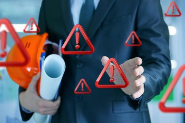 İnşaat güvenliği kuralları. Uyarı işaretleri görünürken bir inşaat yöneticisi planlar ve bir kask tutar.