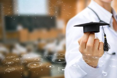 Tıp mezuniyeti. Bir öğrenci gururla mezuniyet şapkasını umut ve bilgiyle dolu bir sınıfta tutar..