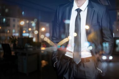 Şehir akşam stili. Bir iş adamı, takım elbisesiyle güvenle durur ve gece boyunca şehrin ışıklarına bakar..