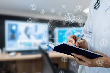 Doktor verileri inceliyor. Bir doktor klinikteki bir ekranda tıbbi verileri incelerken not alır..