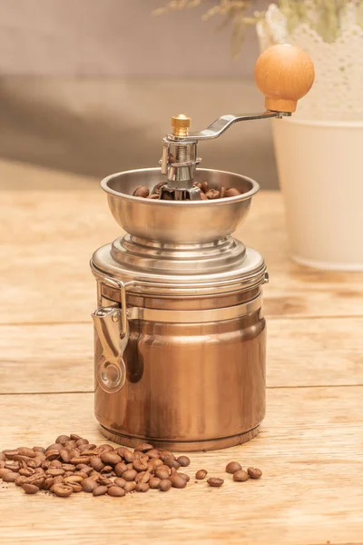 銅とクロムの手動金属製のコーヒーグラインダーの上部に全体のコーヒー粒を持つビューを閉じる 最小限の周囲 テーブルの上にこぼれた穀物と背景に植物の鍋と — ストック写真