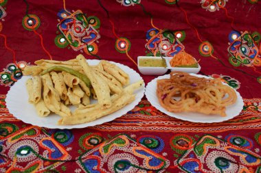 Popular sweet dish Jalebi searved during Indian kite festival of Uttarayan or makar sankranti in gujarat. Decorated with miniature kites, miniature lantern tuggal, ppipudi horn whistle on red background clipart