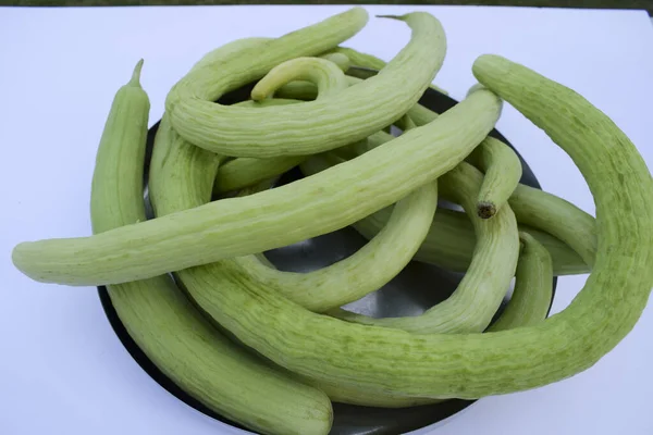 Yard-long snake cucumbers heap, very long thin curvy light green cucumber bunch on white background.