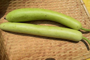 Şişe kabakları ya da kabak olarak da bilinen beyaz çiçek kabakları uzun ve ince kavunlardır. Bambu hasır arka planda Hint Asya sebzeleri