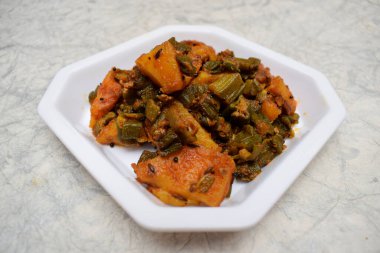 Beyaz arka planda beyaz tabakta servis edilen Hint körili patatesle karıştırılmış bhindi aloo sabji veya Ladyfinger bamyasının üst görüntüsü. Lezzetli Hint yemekleri. Öğle ve akşam yemeği için garnitür.