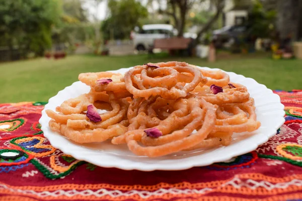 Popüler ve geleneksel tatlı yemek Jalebi ya da kahve kabında kızartılmış gül yapraklarıyla süslenmiş açık hava ve doğa arka planlı.