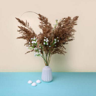 Vazodaki beyaz çiçekli ve kremalı otlar. minimalizm