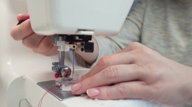 Orta yaşlı bir kadının elleri modern bir dikiş makinesine kumaş dikiyor. Terzi işte.