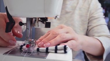 Orta yaşlı bir kadının elleri modern bir dikiş makinesine kumaş dikiyor. Terzi işte.