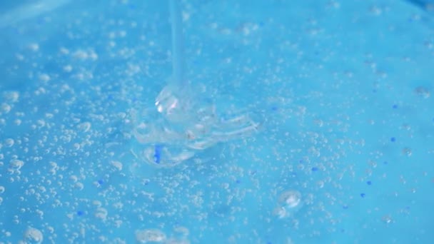 Хитрость прозрачного косметического геля с крошечными пузырьками капает на голубую поверхность. Сыворотка для лица Антивозрастной крем гиалуроновая кислота — стоковое видео