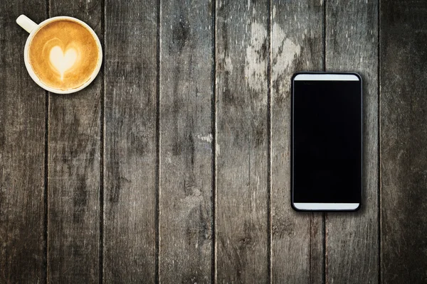 Handy und Kaffeetasse auf Holztisch im Büro — Stockfoto