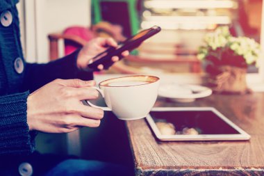 coffee on hand and playing smartphone in coffee shop