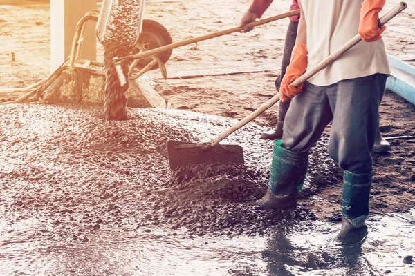 man workers spreading freshly poured concrete mix on building wi