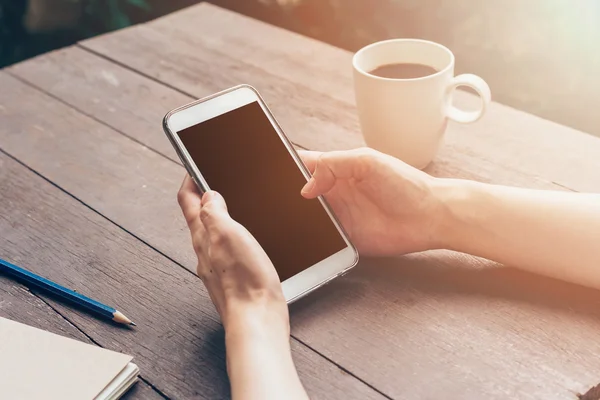 Kvinna hand håller telefonen och använder telefonen på bordet i trädgården vid c — Stockfoto