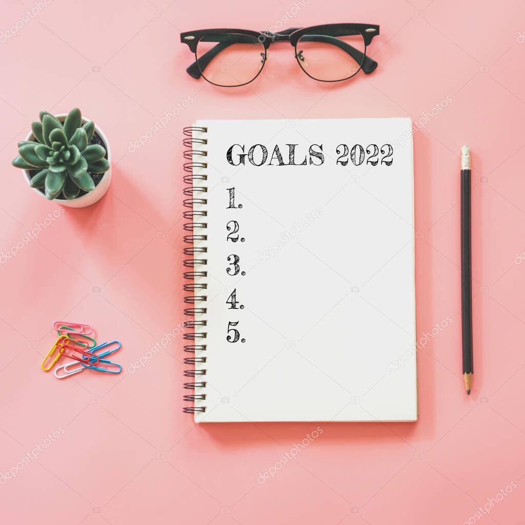 2022 New year concept. Goals list in notepad, smartphone, stationery on pink pastel color with copy space