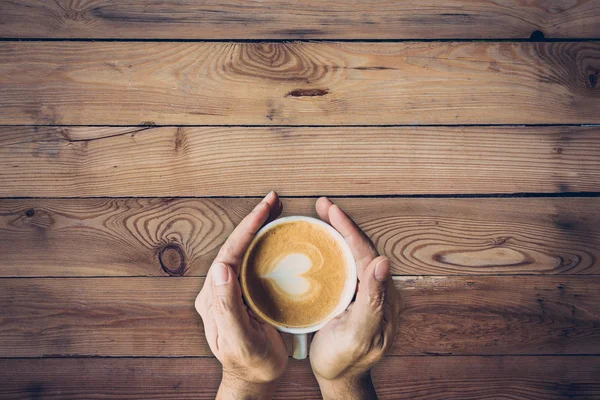 Man hand met warme kop van koffie, met hart vorm op houten t — Stockfoto