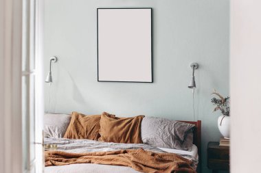 Adaçayı rengi yeşil duvarda siyah portre çerçevesi modeli. Beyaz kapıdan yatak odası manzarası. Ahşap yatakta gri keten ve paslı muslin yastıklar. İskandinav iç mimarisi. Kuru otlu seramik vazo.