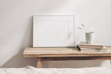 Horizontal white frame mockup on vintage wooden bench, table. Ceramic mug with dry Lagurus ovatus grass and books. White wall background. Scandinavian interior room design. Selective focus.