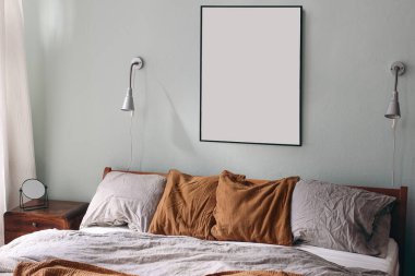 Portre siyah çerçeve modeli ve adaçayı rengi yeşil duvarda gümüş lambalar. Yatak odası manzaralı. Ahşap yatakta gri keten ve paslı muslin yastıklar. Retro komodindeki ayna. İskandinav iç mimarisi.