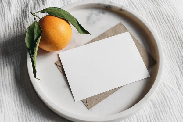 Yaz düğün kırtasiyesi sahnesi. Boş tebrik kartı, davetiye. Zarf zarfı ve portakal meyvesi zarif mermer tepside. Beyaz muslin masa örtüsü arka planı. Üst görünüm. — Stok fotoğraf