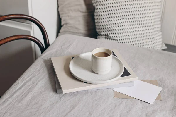 Ontbijt stilleven. Kopje koffie, tijdschrift en wenskaart mockup op beige linnen tafelkleed. Scandinavisch interieur. Wazig eetkamer achtergrond met oude stoel en tafel. — Stockfoto