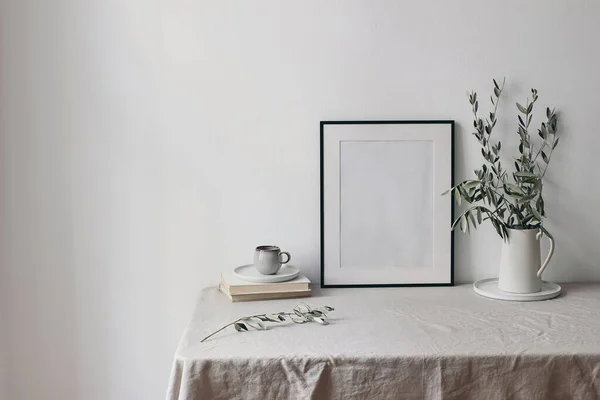 Spring, summer breakfast still life scene. Cup of coffee, books and empty black picture frame mockup. Beige linen tablecloth. Olive tree branches in ceramic jug. Farmhouse, Scandinavian interior. — Stock Photo, Image