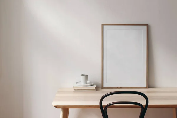 Reggeli csendélet jelenet. Egy csésze kávé, könyvek és üres képkeret mockup a fa asztalon, asztalon. Elegáns munkaterület, otthoni iroda koncepció. Skandináv belsőépítészet. Szoba a napfényben. — Stock Fotó