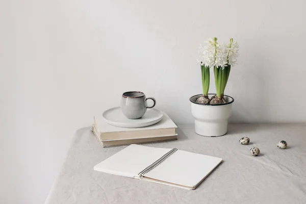 Paaslente stilleven. Kopje koffie, boeken en open dagboek mockup op linnen tafelkleed. Witte hyacint in bloempot. olijftakken met kwarteleitjes. Het concept van thuiskantoor. Scandinavisch interieur. — Stockfoto