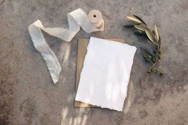 Summer wedding stationery, birthday mock-up scene. Blank greeting card, white silk ribbon and olive tree branches. Grunge concrete background in sunlight, long shadows. Flat lay, top view. — Stock Photo, Image