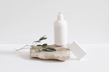 Hafif arkaplanda kozmetik ürünler seti. Şampuan için beyaz plastik pompa şişesi, taş podyumda losyon modeli. Boş sabun kutusu. Yeşil canlı ağaç dalı. Sağlıklı kozmetoloji, spa tedavisi konsepti.